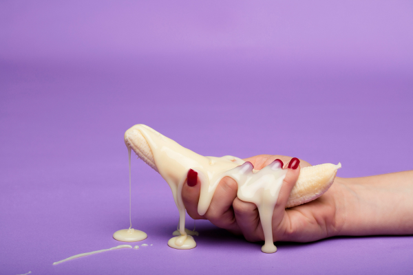 Banana con crema bianca che cola: rappresentazione ironica della domanda “ingoiare lo sperma fa male?”