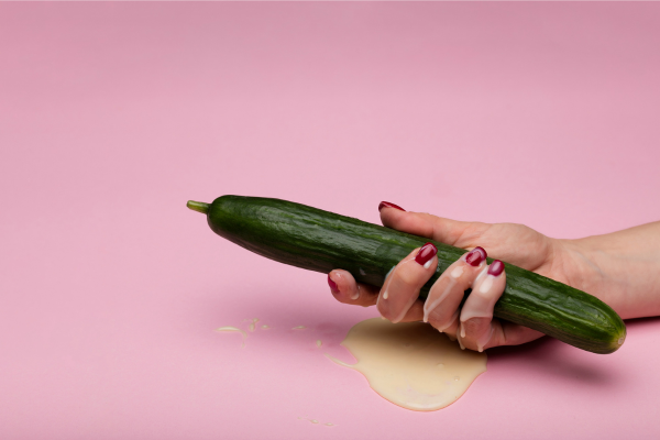 Donna con cetriolo da cui cola della crema: immagine ironica per illustrare i benefici dell’ingoiare lo sperma